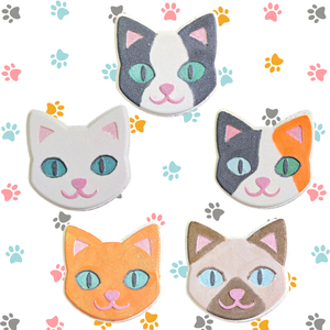 5 different Kitty Face Bath Bombs painted in a variety of cat colors and breeds. There is a background of cat paws in the background.