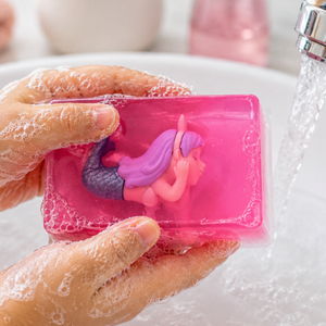 Pink soap with a mermaid figurine held by a hand under running water.