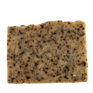 A rectangular bar of handmade soap with a speckled pattern of dark brown and black flecks on a light beige base, isolated on a white background.